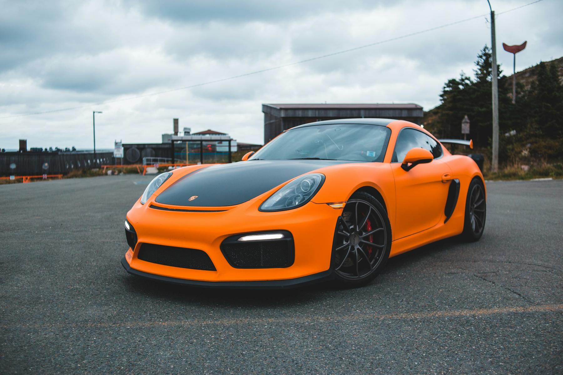 Satin orange color change wrap on a Porsche Cayman under an overcast sky