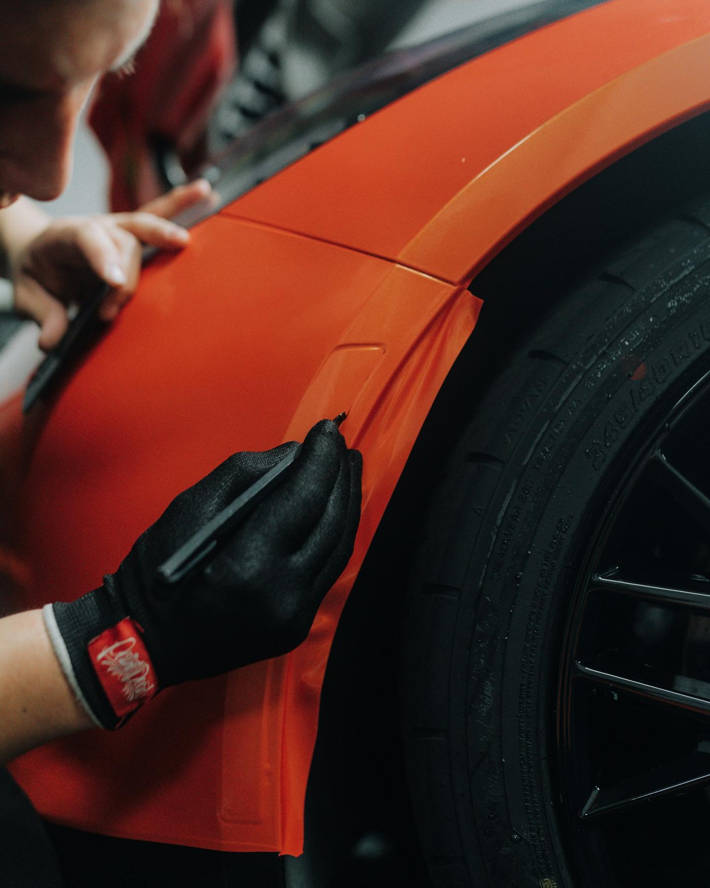 Installer trimming orange vinyl around a wheel arch