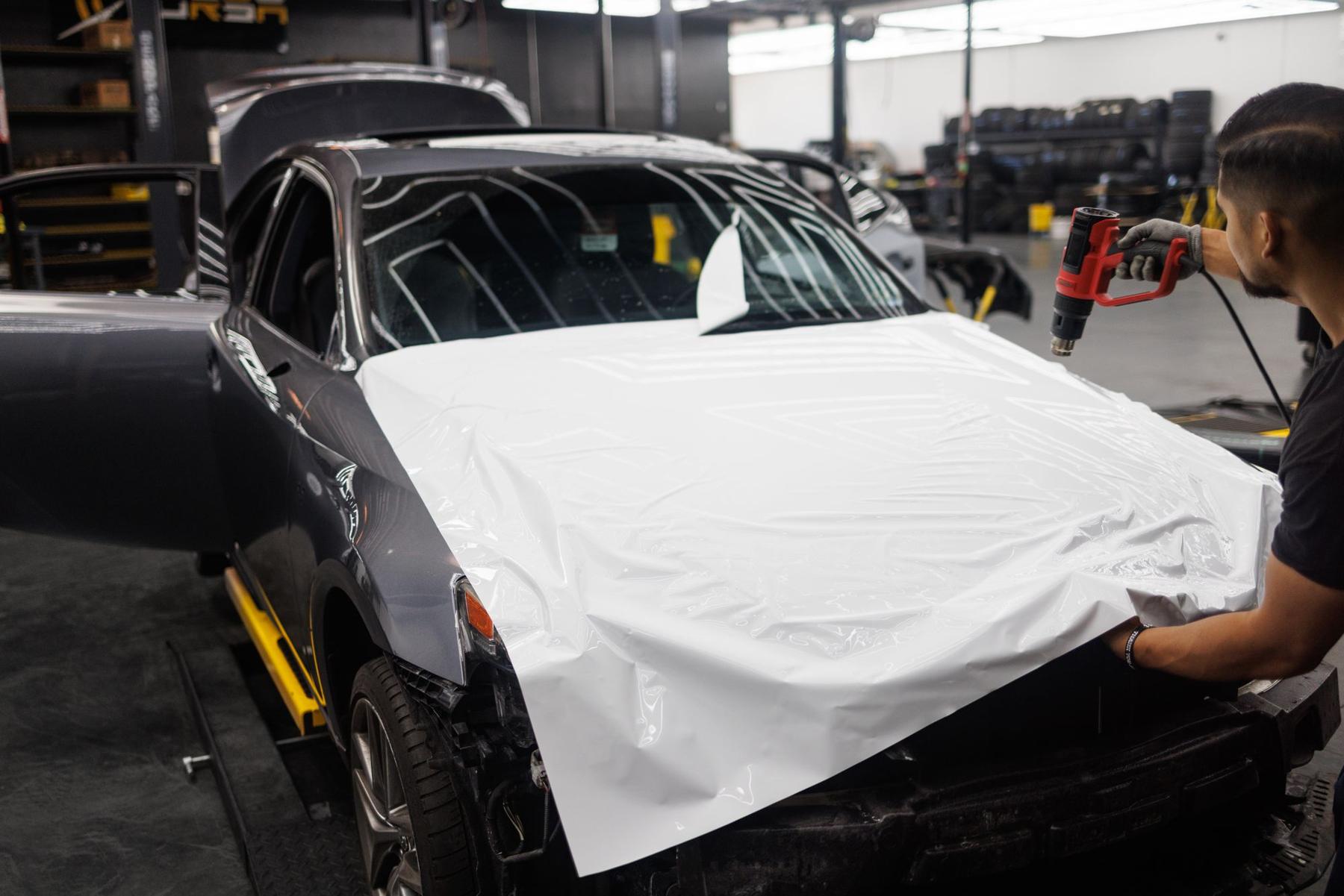 Sports car with fresh white vinyl laid across the hood in a wrap shop